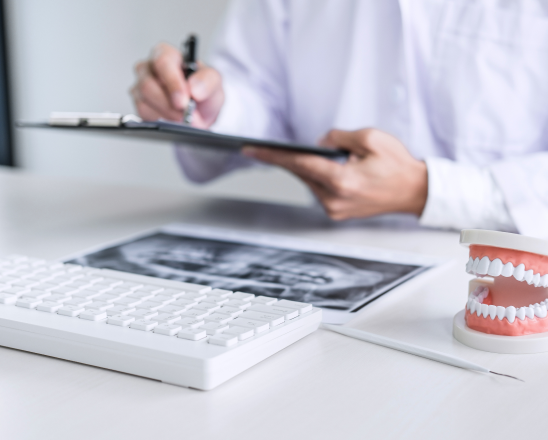 Dentist reviewing dental X-ray and patient records on clipboard at desk.